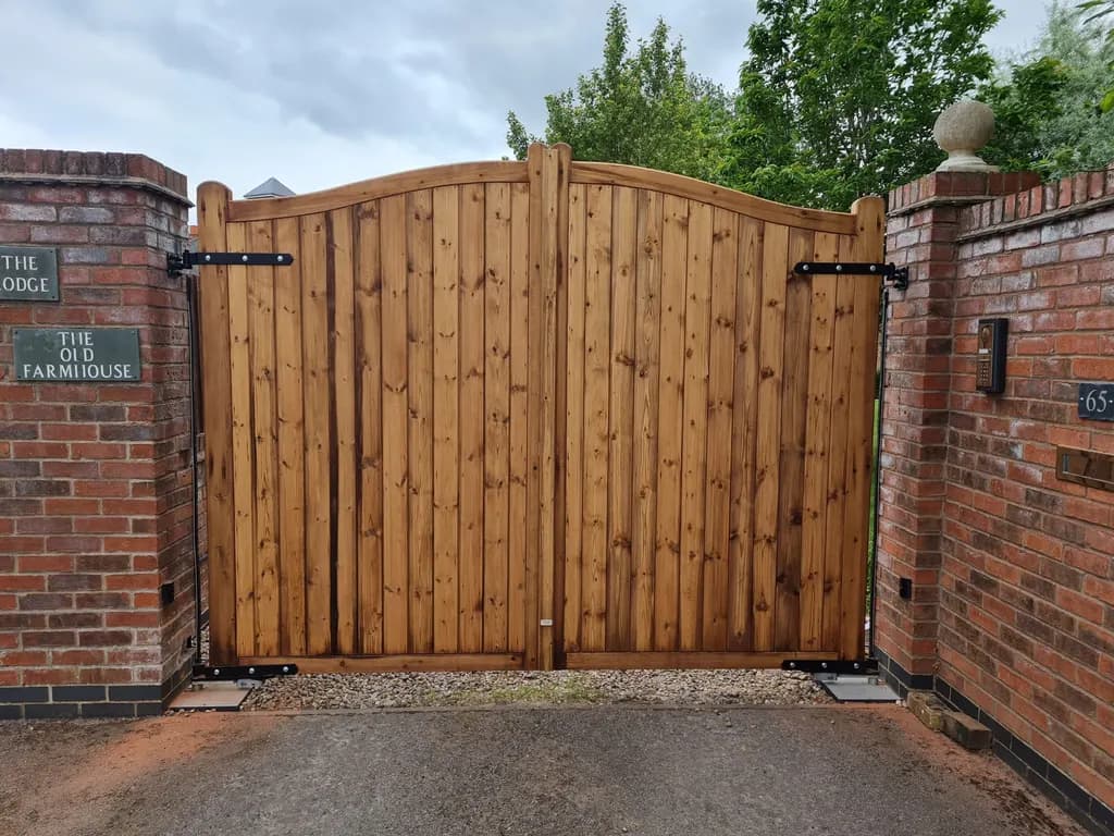 Arched timber gates hung between brick piers at a farmhouse entrance