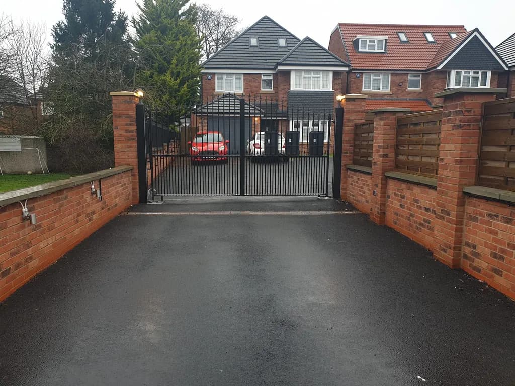 Black bar gates set into a brick boundary wall at a large house