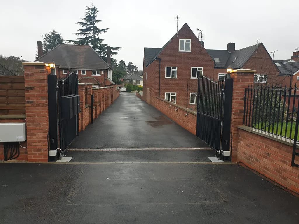 Black bar gates opening onto a long private drive between brick walls