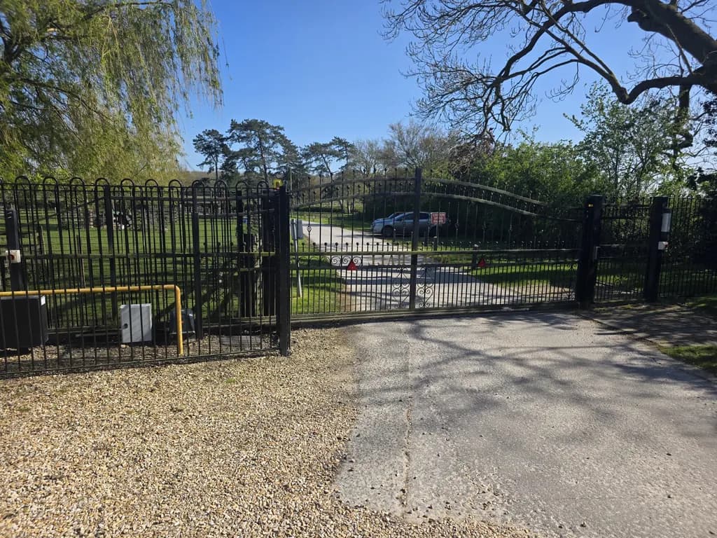 Black vertical-bar swing gates on a gravel entrance to a rural property