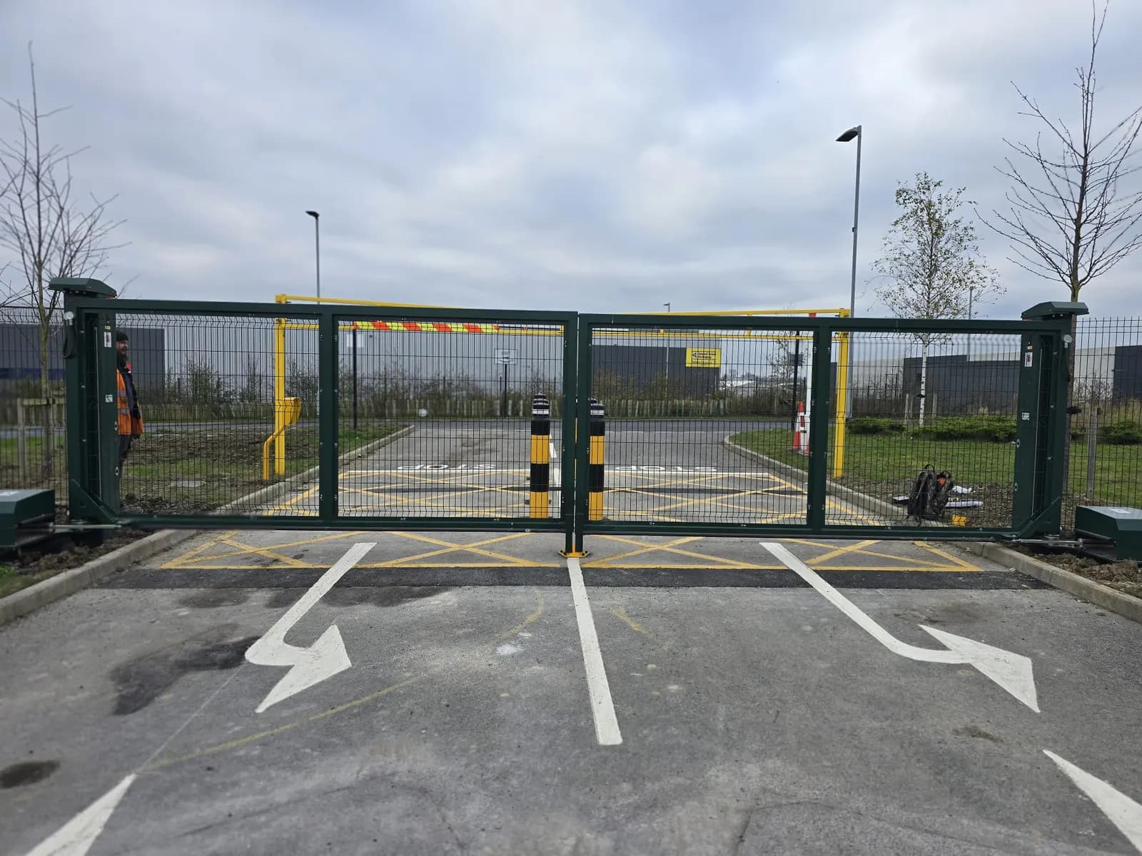 Green barrier and protective bollards at a car park entrance with directional road markings