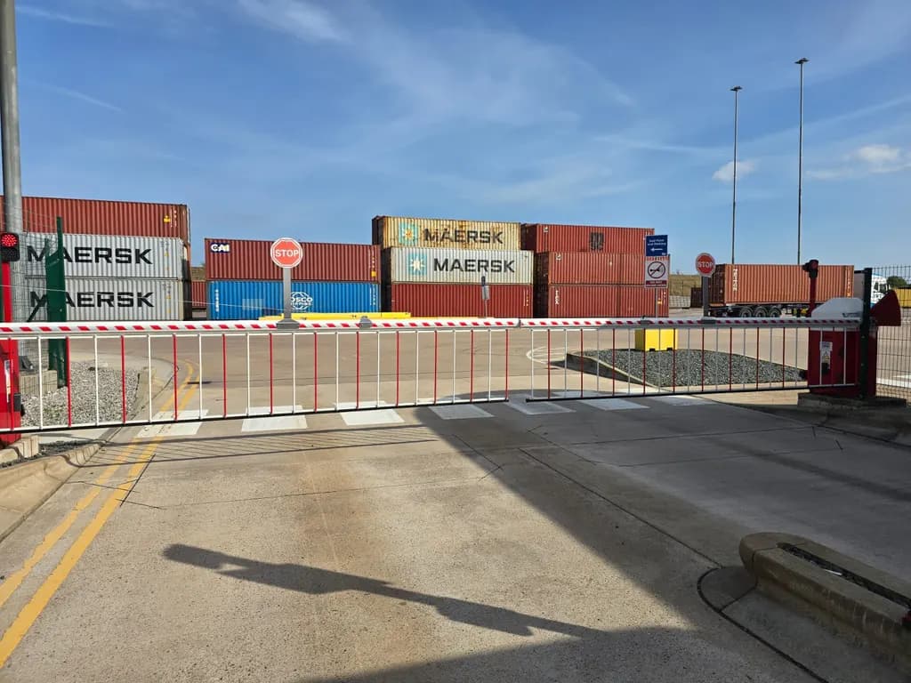 Barrier-controlled lane at a container terminal, with stacked shipping containers behind