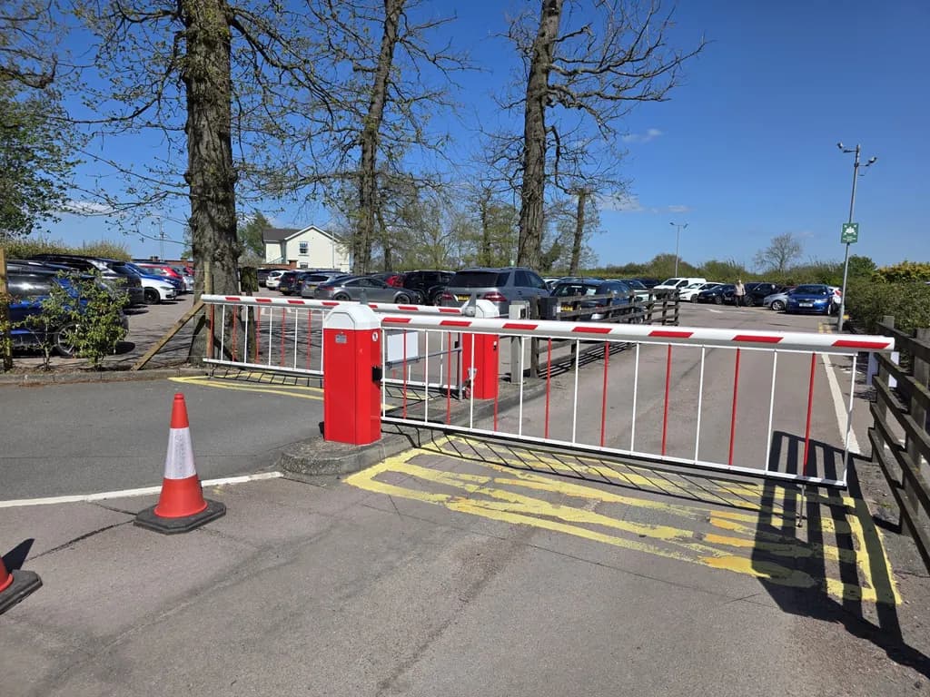 Red and white rising-arm barriers controlling a car park entrance, with pedestrian guardrail segregating the footway