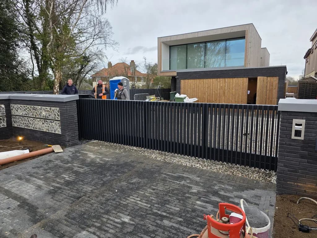 Black bar gate and matching railings at a contemporary home, with a flush-mounted entry keypad on the pier