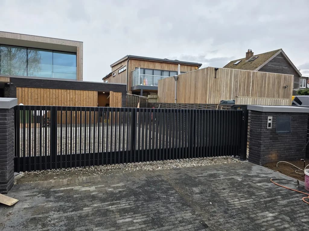 Vertical-bar boundary railings and automated gate across a new block-paved driveway