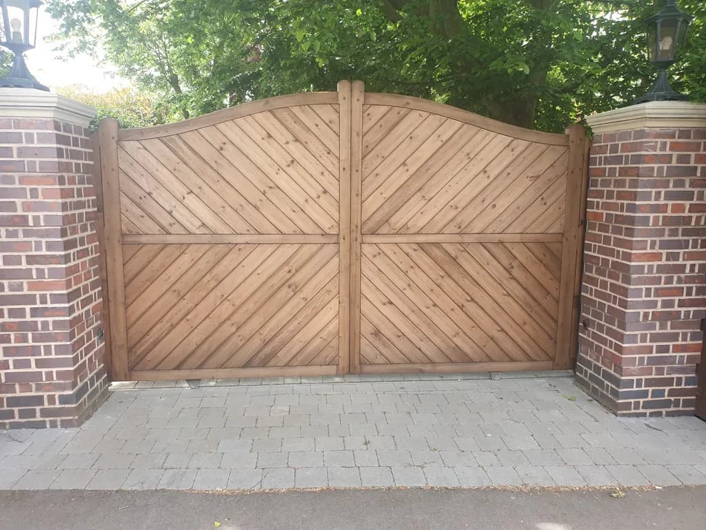 Curved-top timber gates between brick piers on a paved drive