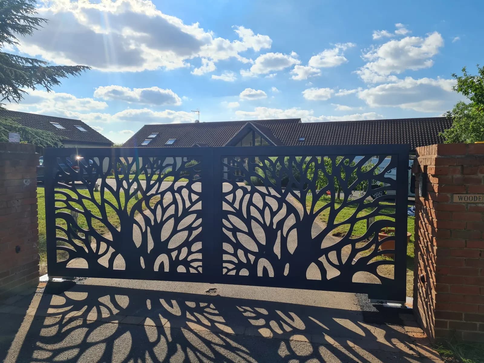 Decorative laser-cut steel gates between brick piers, casting patterned shadows on the drive