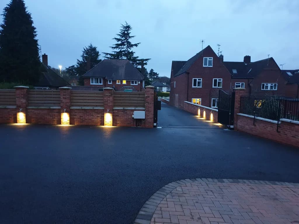 Automated gates at dusk with the brick piers lit by ground-level uplighters