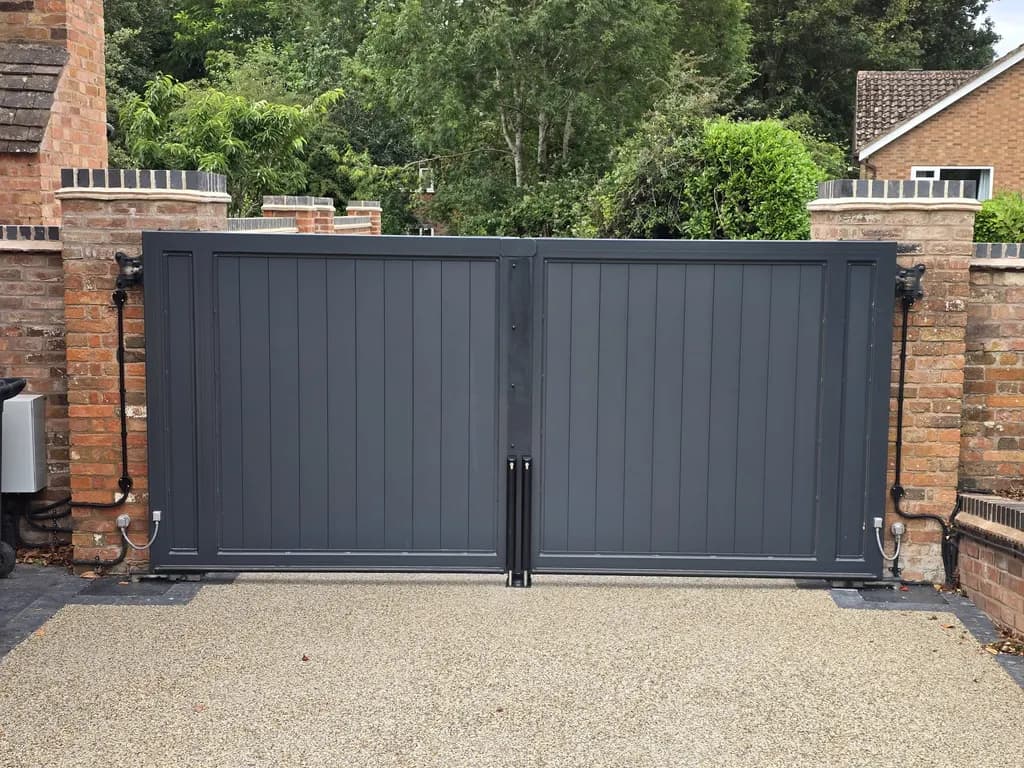 Grey panelled swing gates hung between brick piers on a resin driveway