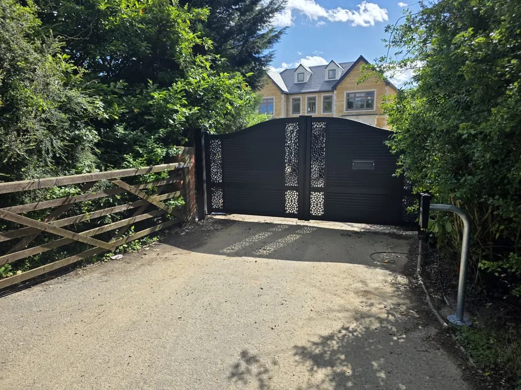 Dark gates with laser-cut decorative panels across a gravel driveway