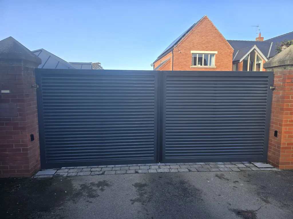 Grey slatted double gates between brick piers at a modern home