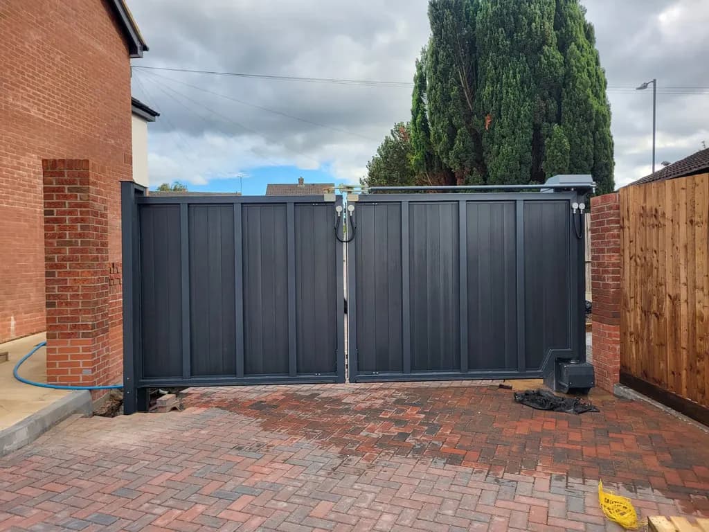 Grey slatted swing gates with the ram operator visible, on a brick-paved driveway