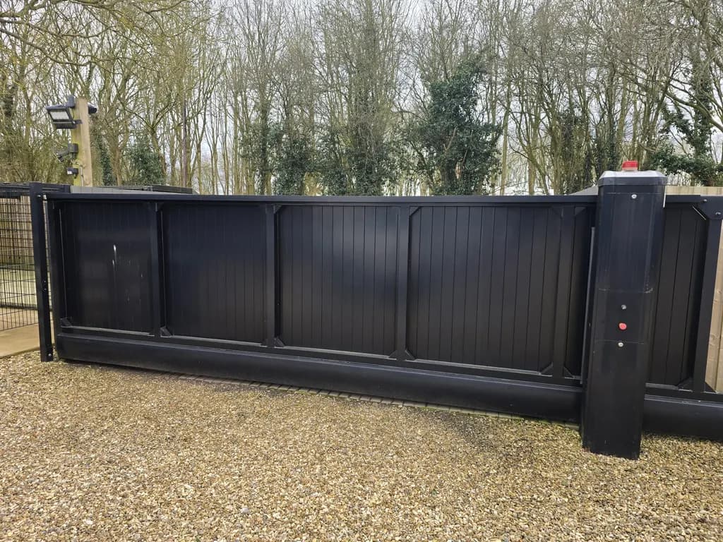 Dark slatted sliding gate and operator column on a gravel drive