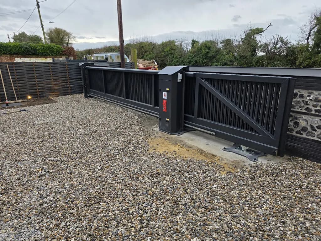Automated sliding gate set into a flint boundary wall on a gravel entrance