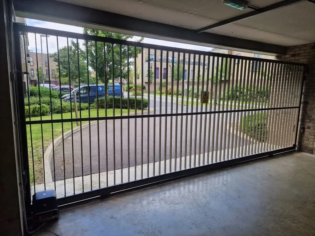 Bar-infill sliding gate controlling undercroft parking beneath a building