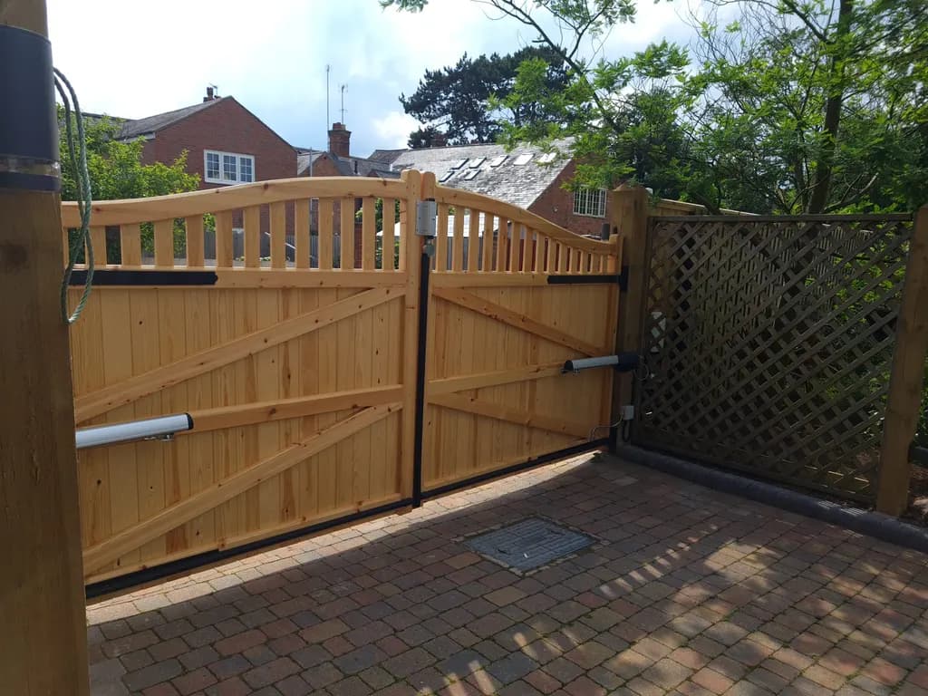 Timber gates with ram operators on a block-paved drive, with lattice fencing alongside